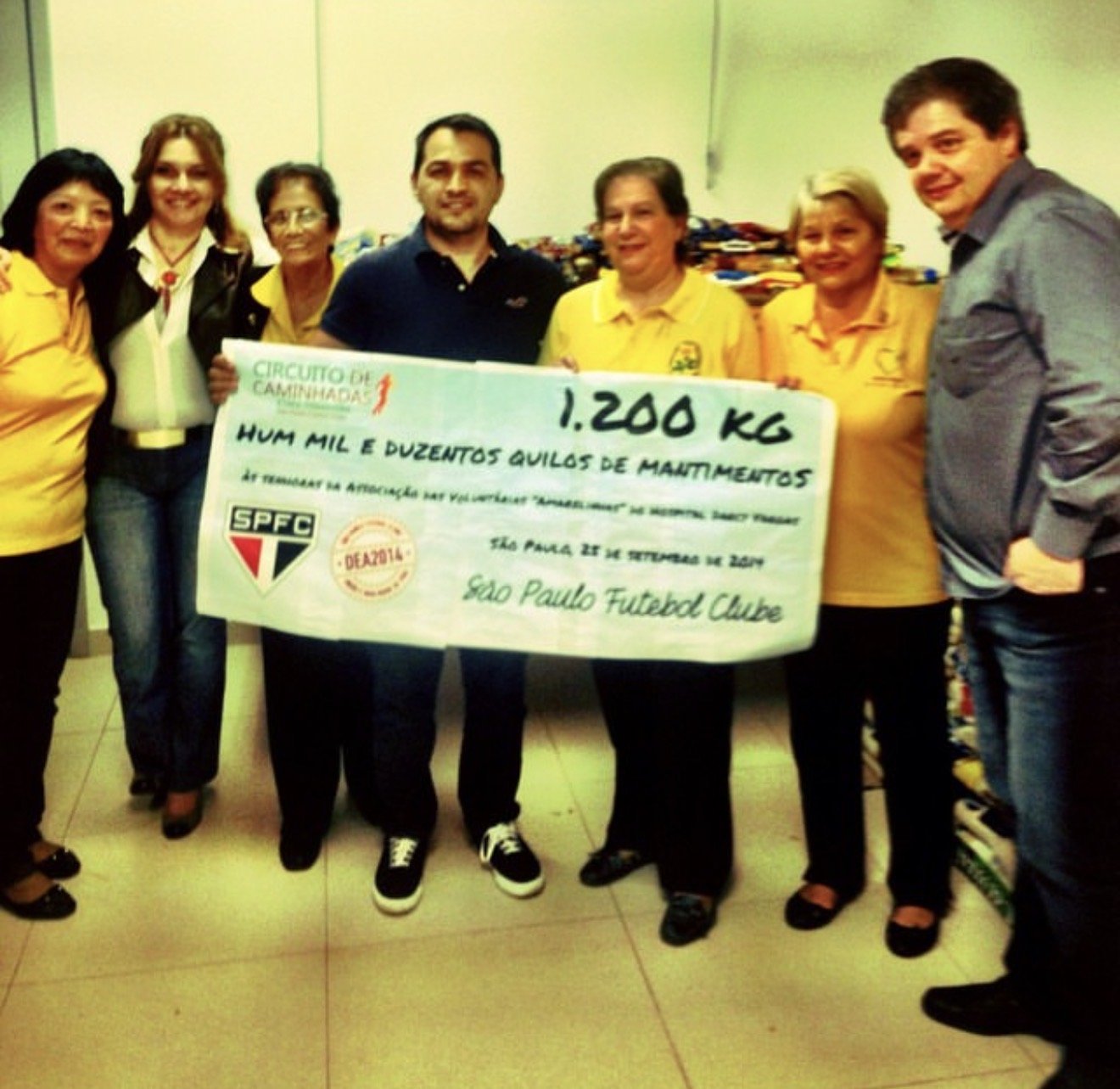 Jura e voluntárias segurando um cheque simbólico de 1.200 kg de mantimentos arrecadados pelo Circuito de Caminhadas do São Paulo FC