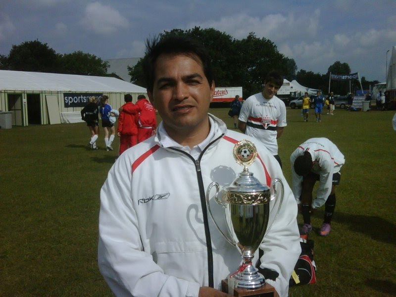 Jura segurando um troféu em um torneio de base, com jogadores de uniforme do São Paulo FC ao fundo